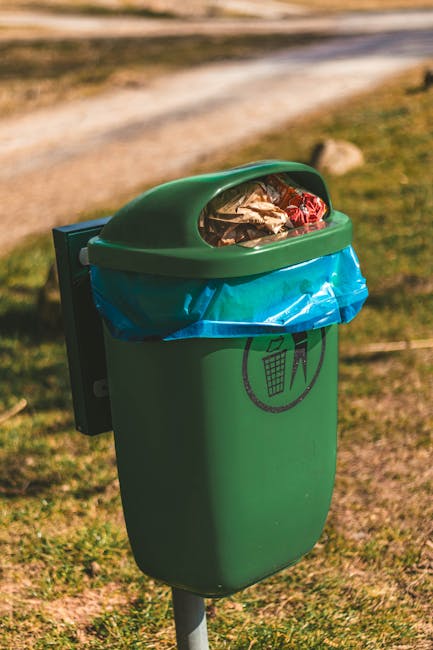 Close-up image of black plastic rubbish bags made from glossy, flexible material, tightly tied at the top with visible creases and folds, stacked together against a plain, light-colored wall or backgr